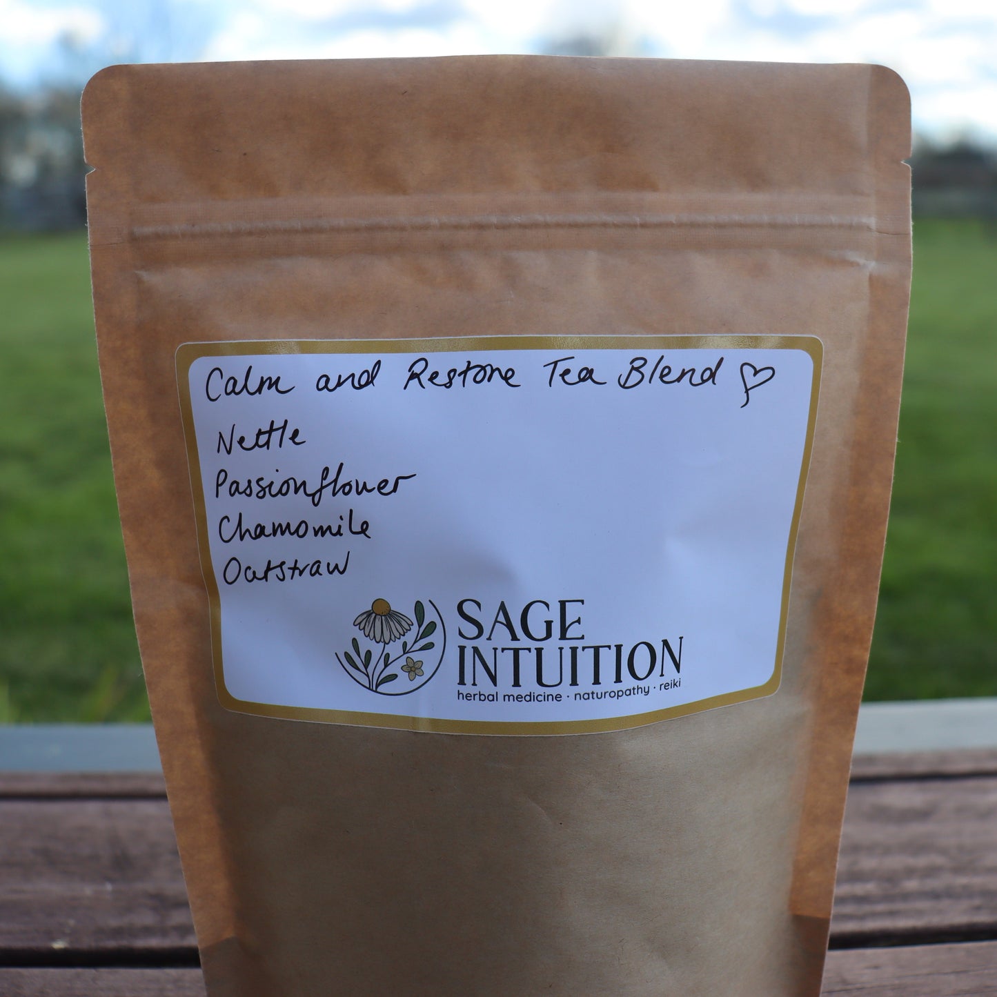 Tea blend package with 'Sage Intuition' label on a wooden surface with grass and sky in the background