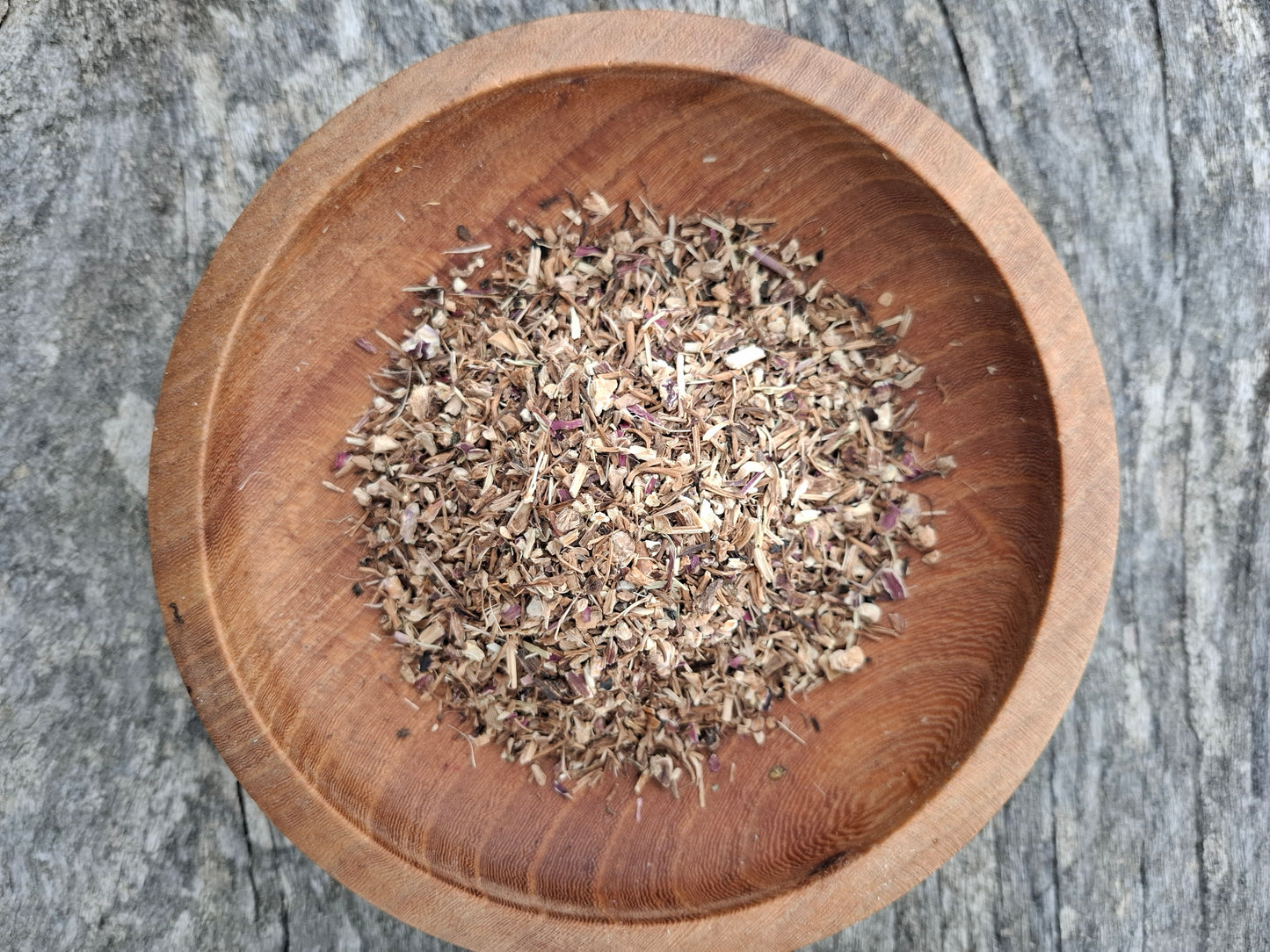 Wooden bowl with dried herbs on a textured surface