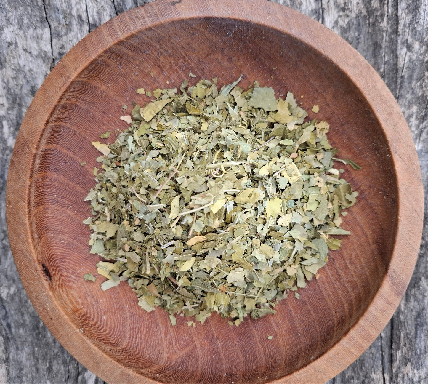 Dried herbs in a wooden bowl on a rustic wooden surface