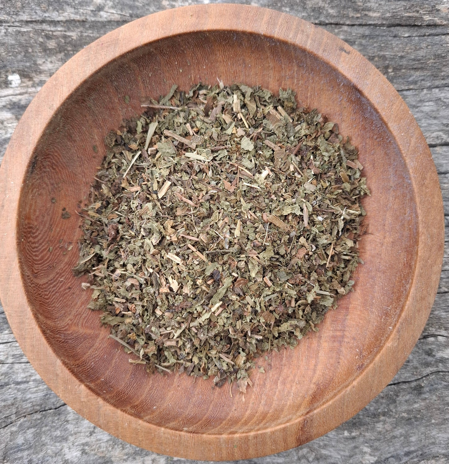 Wooden bowl filled with dried herbs on a wooden surface