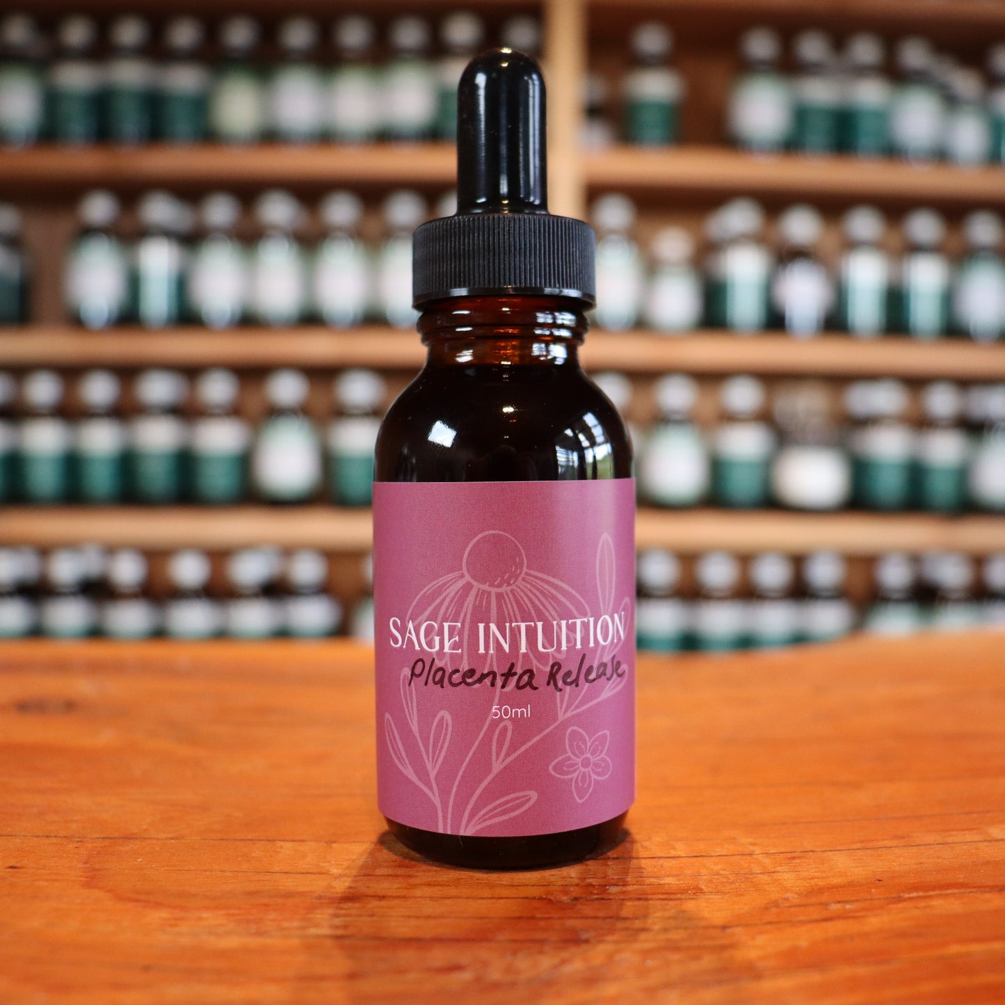 Bottle of Sage Intuition placenta release tincture on a wooden surface with shelves of similar bottles in the background.