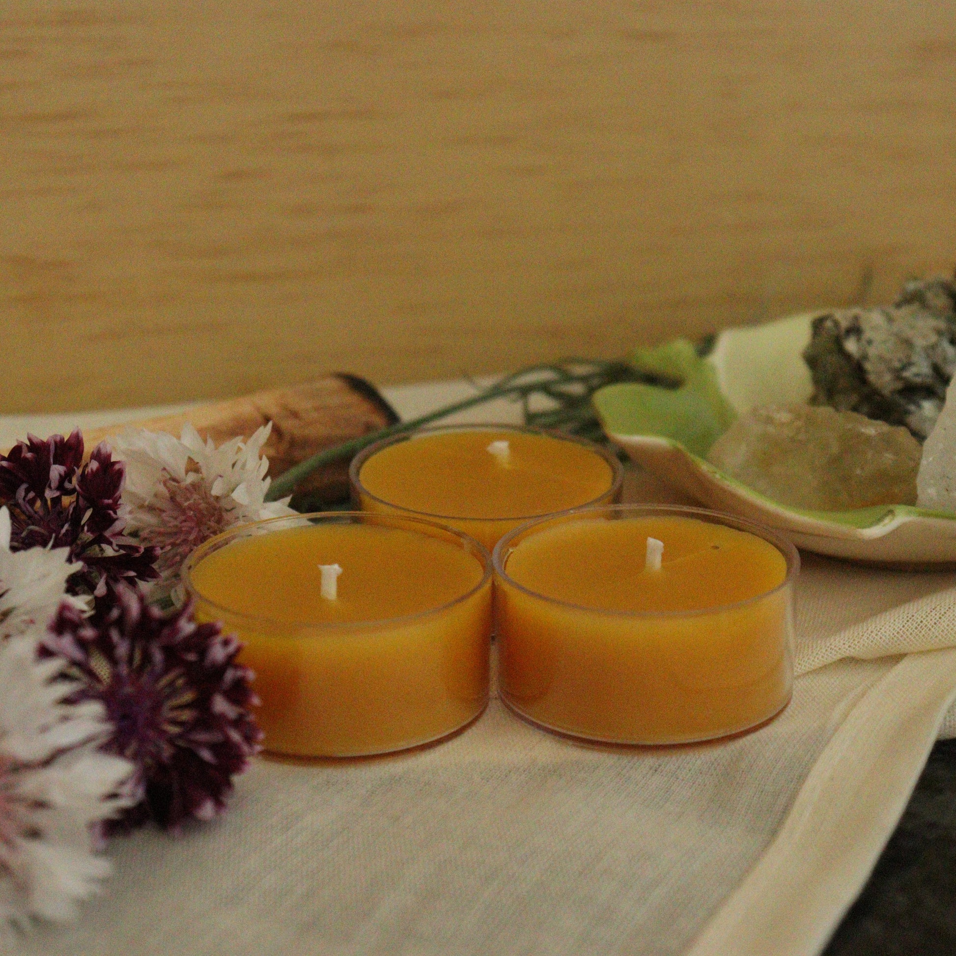 Three small orange candles on a wooden surface with flowers and a crystal.