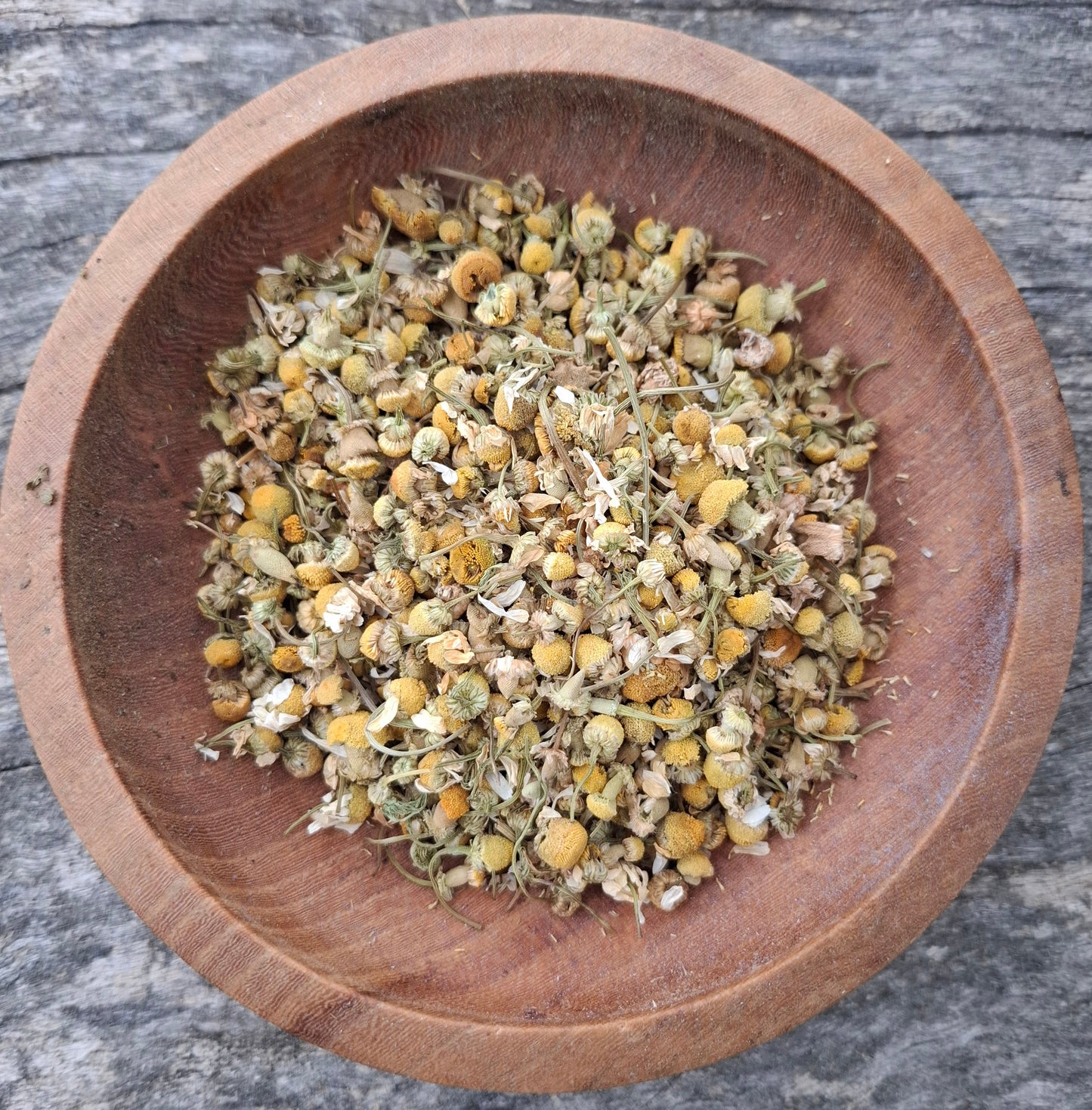 Dried herbs in a wooden bowl on a rustic wooden surface