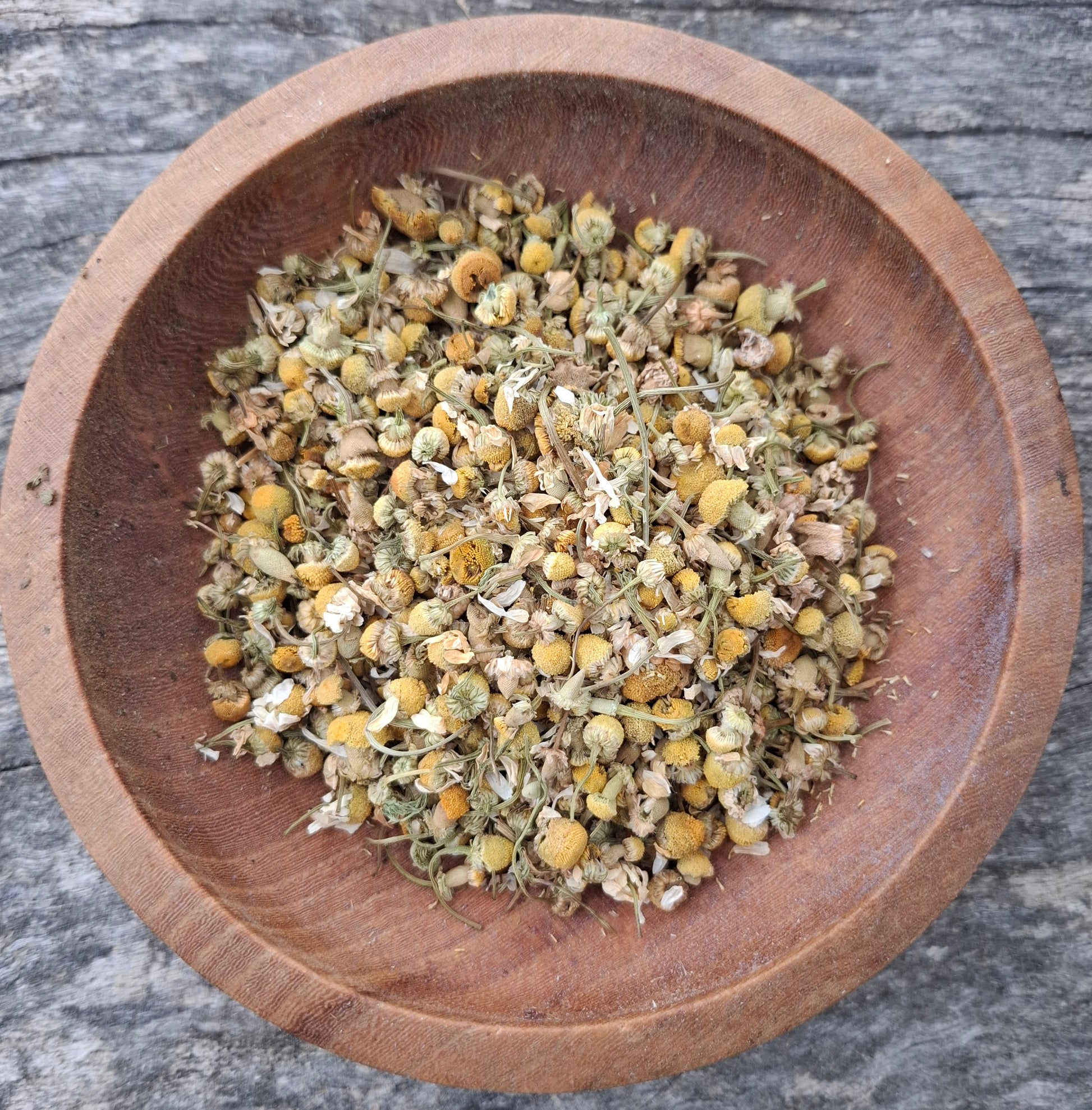 Dried herbs in a wooden bowl on a rustic wooden surface