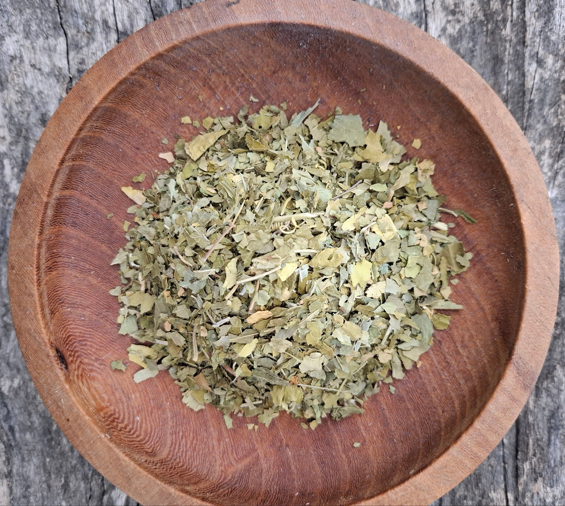 Dried herbs in a wooden bowl on a rustic wooden surface