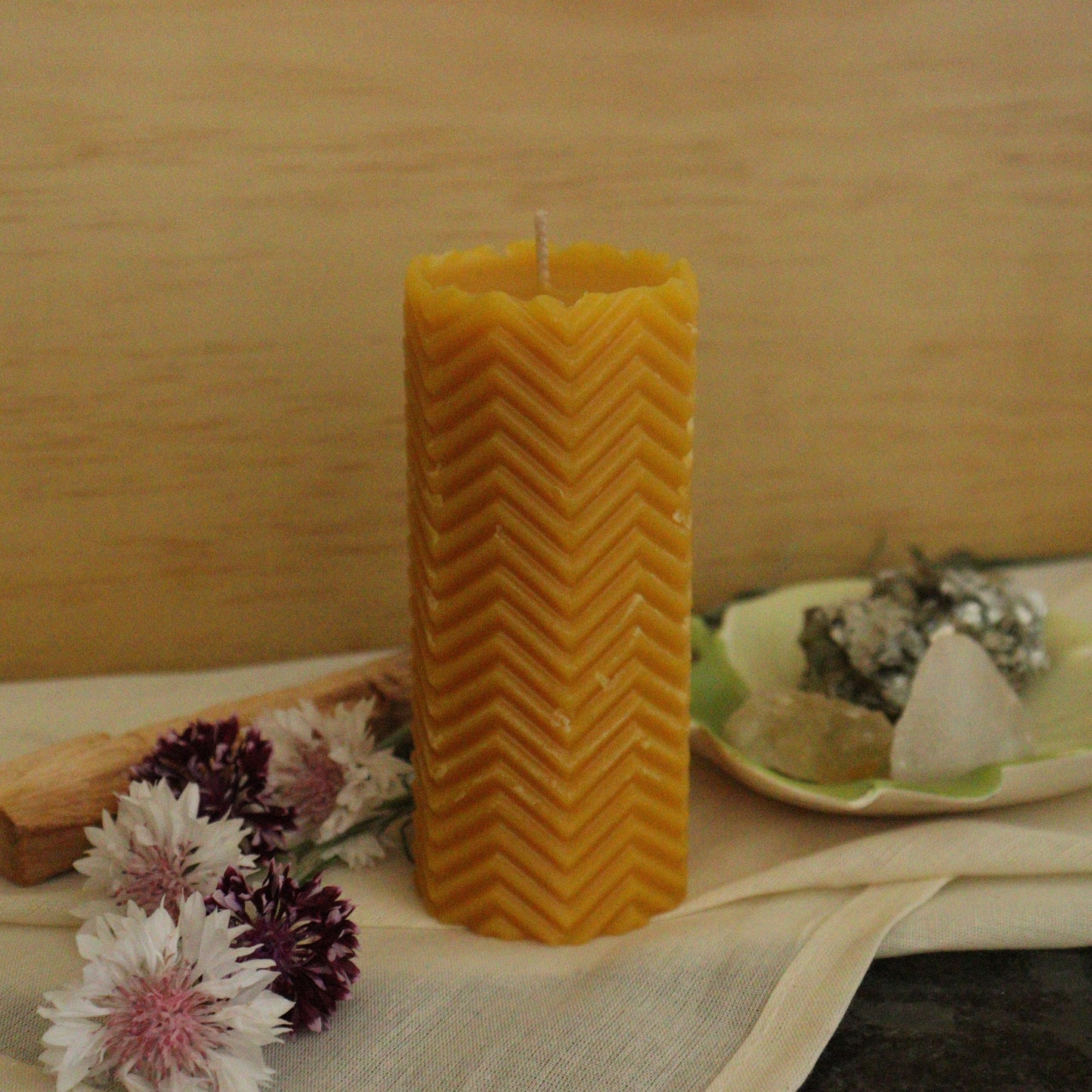 Beeswax candle with zigzag pattern on a wooden surface with flowers and a plate.